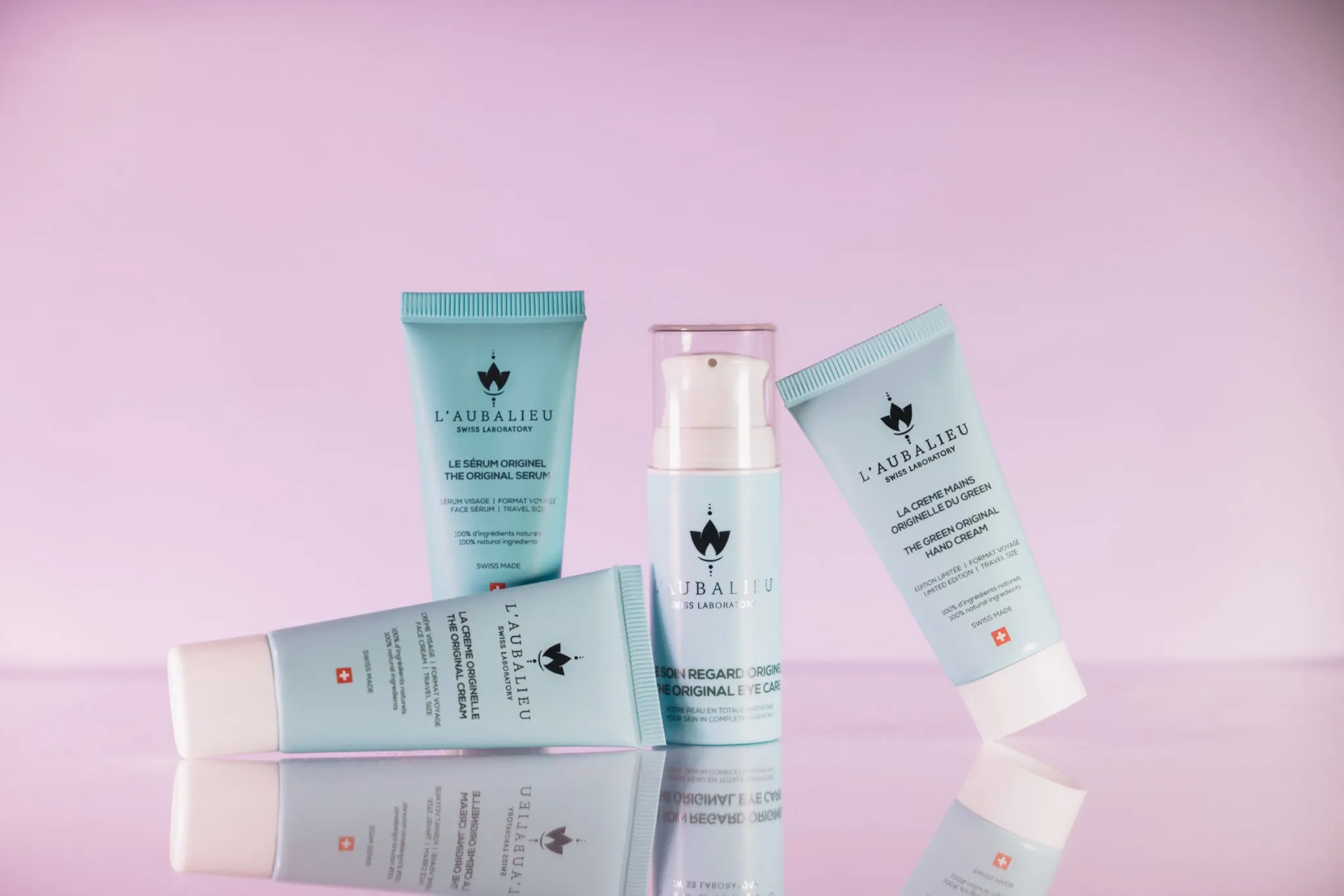 Assortiment de produits de soin L'Aubalieu en format voyage sur fond rose.